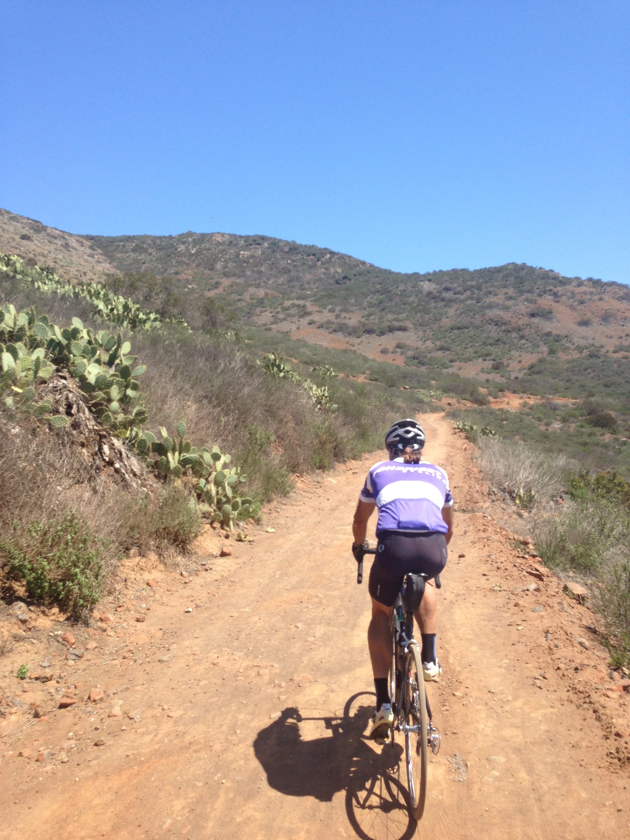 Don riding up a dirt climb. I like the cactus all around.